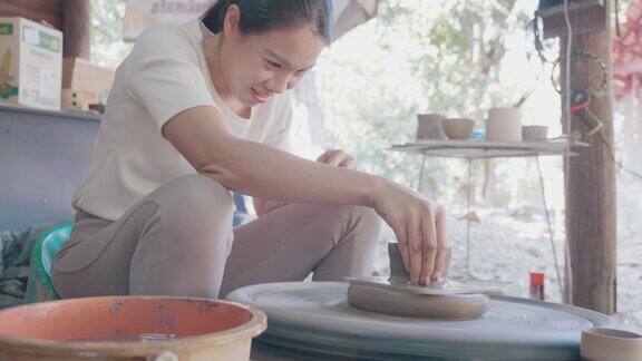 亚洲妇女粘土艺术家在她的工作室与纺纱陶轮工作