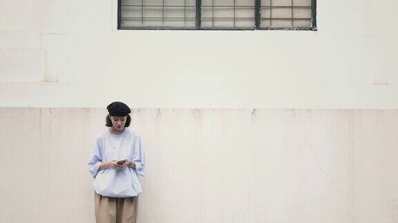 亚洲华人年轻女子倚在街墙上等待