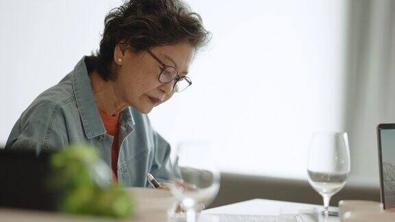 亚洲华人老年妇女打字与笔记本电脑在餐桌网上购物