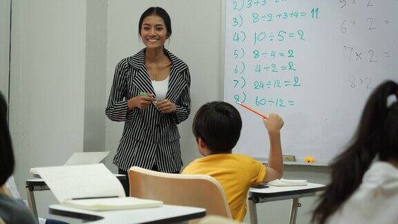 亚洲老师在学校的教室里教孩子们小男孩和小女孩一起举手接受评论教育理念、经验学习和技能发展