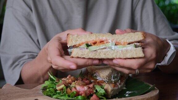 特写镜头:女性的手从木托盘里拿着一个切好的三明治上面有蔬菜和鱼双手向镜头展示三明治的切面