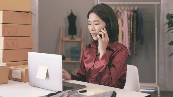 年轻的亚洲女商人一边工作一边打电话一边在家给网上顾客送快递