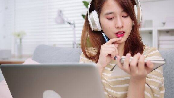 亚洲女大学生看笔记本电脑屏幕看在线课程和做笔记而学习在线