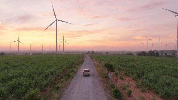 日出或日落时汽车行驶在被风力涡轮机包围的绿色田野的鸟瞰图