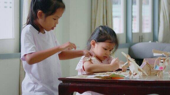 亚洲女孩和她的姐姐正在组装木制玩具上色