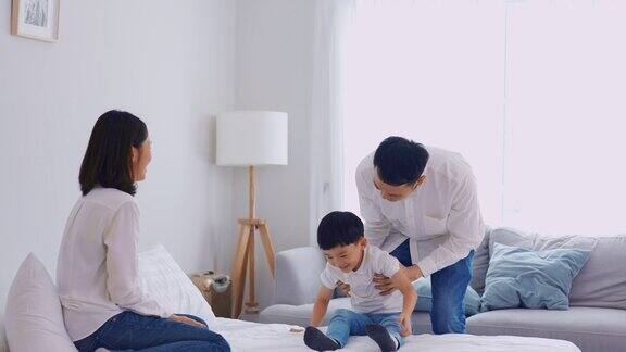 亚洲父母和年幼的儿子在家里的卧室里度过闲暇时光迷人的夫妇和小男孩感到快乐和放松享受一起在床上玩耍家庭-父母关系概念