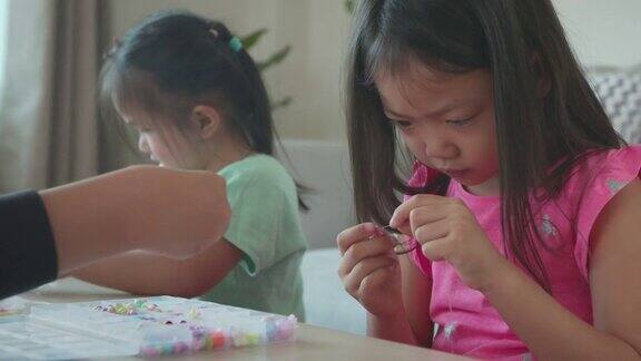 亚洲女孩和朋友把珠子串在一起在家里有意图和乐趣孩子创造手工手镯以发展手的能动性