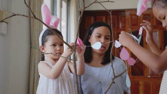 亚洲女孩和父母用花环装饰房间挂在树枝上复活节假期