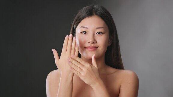 年轻和美丽工作室肖像的年轻亚洲妇女应用宠爱霜在她的手掌保湿的手皮肤