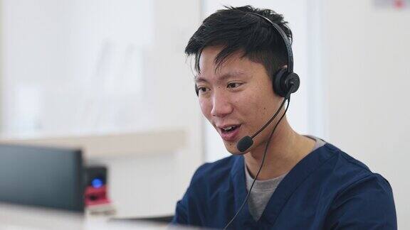 在医院接待柜台接听电话的亚裔华裔男护士接待员