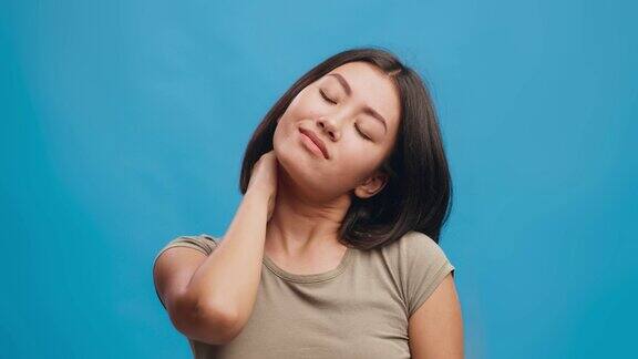 肖像疲惫的年轻亚洲妇女遭受颈部疼痛和按摩颈部蓝色工作室背景