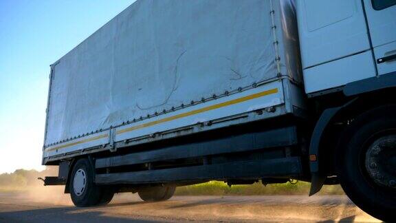 低视野的卡车与货物拖车行驶在高速公路和运输货物在日落时间一辆白色卡车在乡间公路上疾驰后面扬起尘土物流慢动作
