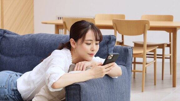 一个亚洲女人在沙发上玩智能手机