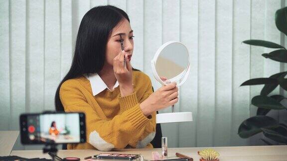 一位亚洲女性一边在社交媒体上直播一边向博客上的朋友解释化妆的方法