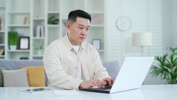 自信专注的亚洲人坐在办公桌前在笔记本电脑上打字