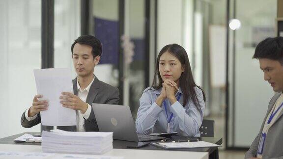 一群年轻的亚洲商人在办公室开会和头脑风暴讨论商业计划并通过笔记本电脑和金融图表文件展示和解释财务图表
