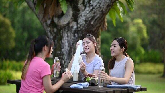 3个亚洲中国年轻女子在公园休息后早上锻炼吃健康的食物和饮料在公园长椅