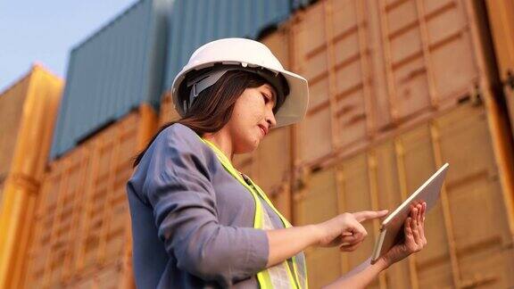 女工程师领班戴安全帽用数字平板电脑与货物集装箱背景
