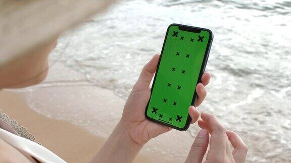 女人用智能手机绿屏海滩
