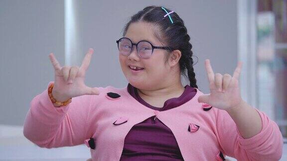 一个15岁的亚洲小女孩戴着眼镜带着唐氏综合症微笑着站在教室里看着摄像机残疾的肖像