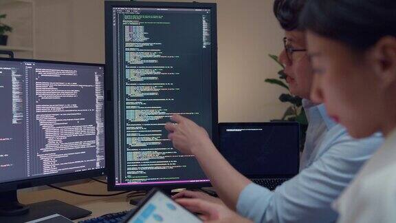一群亚洲人的特写软件开发人员晚上坐在办公室里有多个屏幕的桌子前用电脑写代码程序员开发