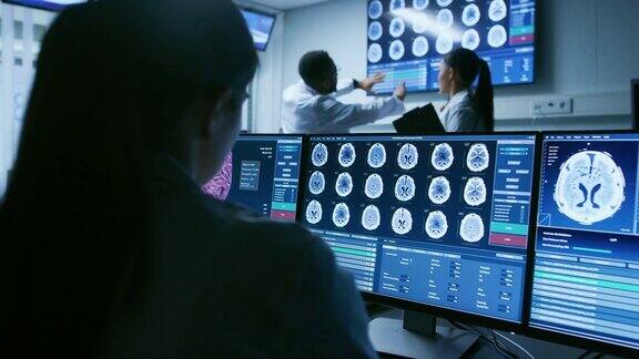 在肩膀上方拍摄的女性医学科学家工作与大脑扫描图像上的个人电脑在实验室神经研究中心致力于治疗脑肿瘤