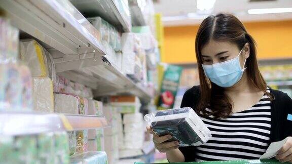年轻的亚洲妇女带着防护口罩在超市购物阅读清单