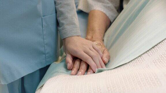护士在病床上抚摸老妇人的手表达对病愈的老年病人的关爱