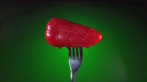 叉子用鲜红辣椒沾上水滴旋转绿色背景宏