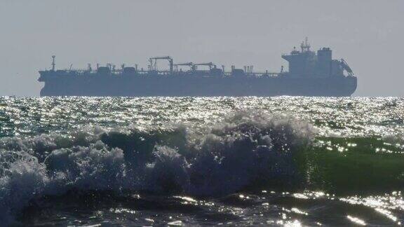 在远处的地平线上有一艘石油(石油)油轮在南加州亨廷顿海滩附近的海浪的慢动作拍摄