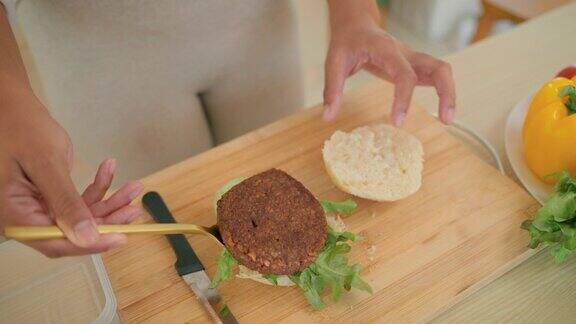女性有色手准备素食汉堡用蔬菜和植物性肉放在木板上作为早餐