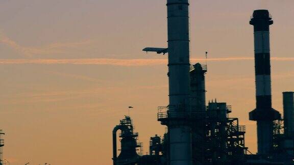 一架飞机在炼油厂后面的日落天空中降落