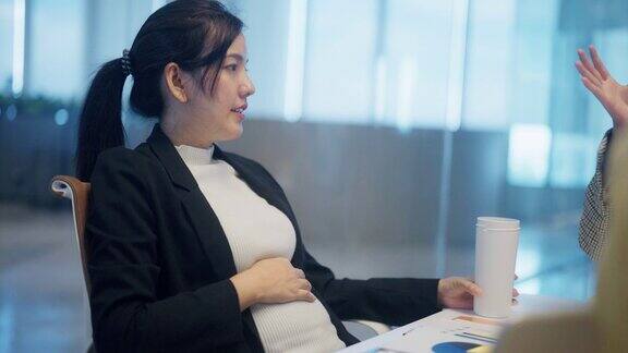 亚洲怀孕经理坐在桌边的侧视图在办公室工作时头脑风暴和揉肚子