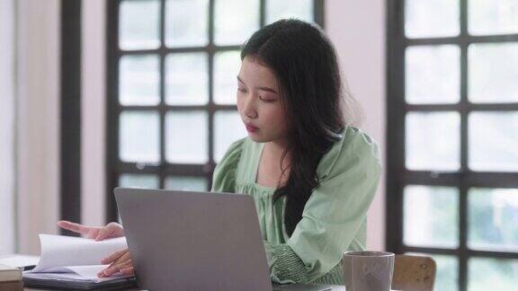年轻的亚洲女性使用笔记本电脑技术打字讲课和在线学习在家里看着屏幕坐在桌子上远程教育