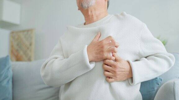 亚洲老年男子胸部疼痛感觉心脏病发作有魅力的老年病人坐在客厅的沙发上因剧烈疼痛而捂着胸口呼吸困难