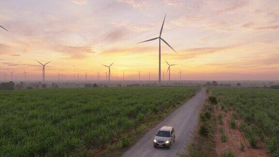 日出或日落时汽车行驶在被风力涡轮机包围的绿色田野的鸟瞰图