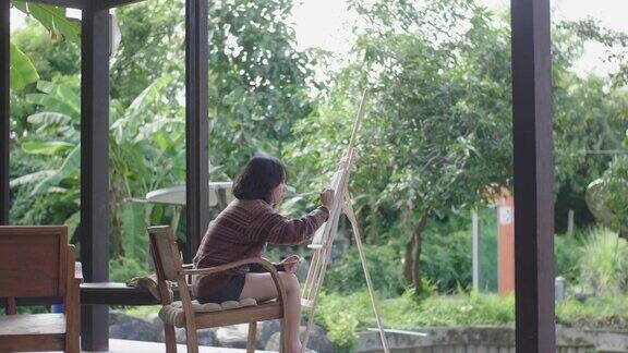 年轻的亚洲女画家在后院用画笔和画架创作艺术品