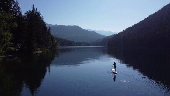 一名女子站在一个原始的高山湖泊上划桨冲浪