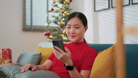 圣诞节那天一名亚洲女子坐在客厅里用智能手机上网休息