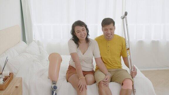 幸福的亚洲女人戴着假肢腿和一对夫妇的腿残疾微笑着看镜头享受躺在床上的爱人拥抱在一起的时刻