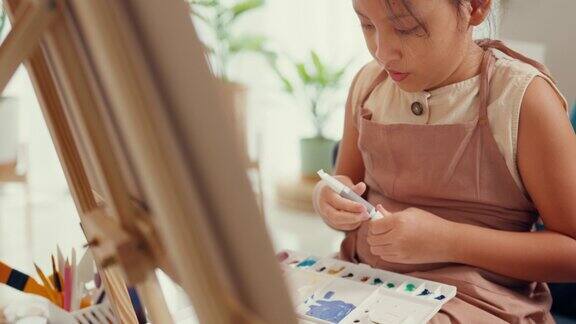 近距离亚洲学步的女孩用围裙坐在沙发椅子前的油画画布把丙烯酸颜色在调色板上使用调色板刀混合颜色在客厅在家里
