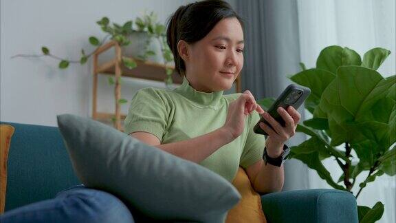亚洲女性坐在家里客厅的沙发上用智能手机上网休息