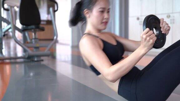 专业美丽的亚洲妇女锻炼做坐起与重量板运动在健身馆健康的生活方式运动员腹肌建立强壮和健康的身体4k分辨率