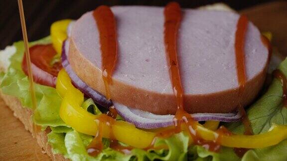 特写把红酱放在火腿和蔬菜三明治上