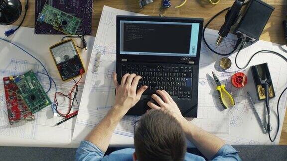 一个天才的IT技术员写代码在他的笔记本电脑坐在他的桌子上他被各种技术组件包围阳光照在他的桌子上