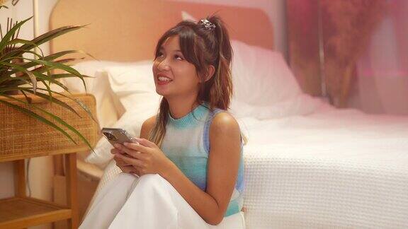 年轻的亚洲女性在卧室里用智能手机上网