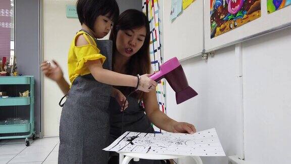 一位亚洲华裔年轻女学生在美术课结束后用吹风机吹干她的水彩画