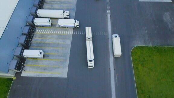 空中拍摄的卡车与挂载半挂车离开工业仓库仓库大楼装卸区的许多卡车装载卸载商品