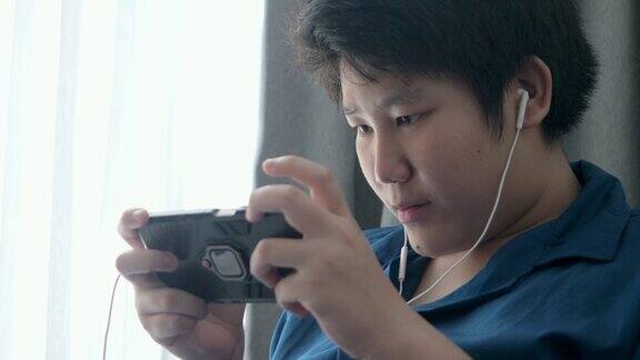 亚洲男孩在家靠窗的沙发上放松玩手机游戏生活理念