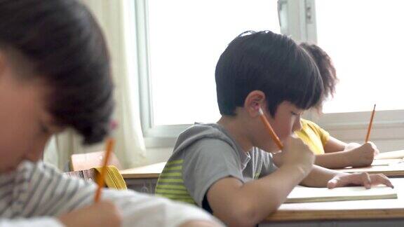 亚洲学校的孩子坐在学校里用铅笔在书上写字学习教育学习男女学生坐在课桌前写笔记本小学年龄的男孩和女孩